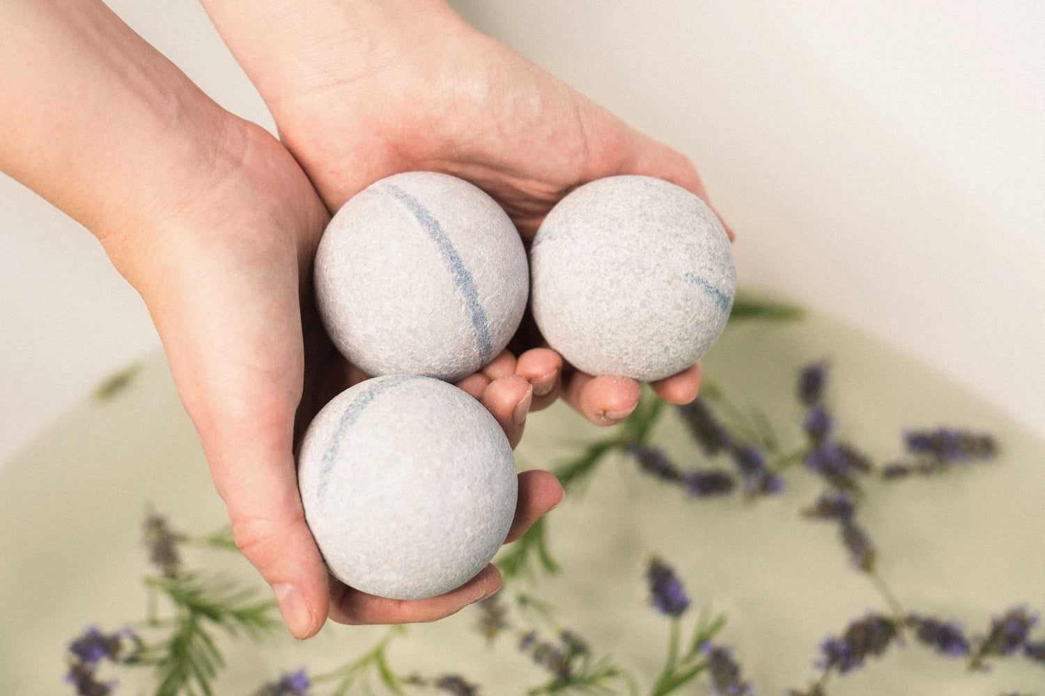 Close-up of three mineral bath bombs held above a bathtub with soft lavender, creating a relaxing aromatherapy spa experience.