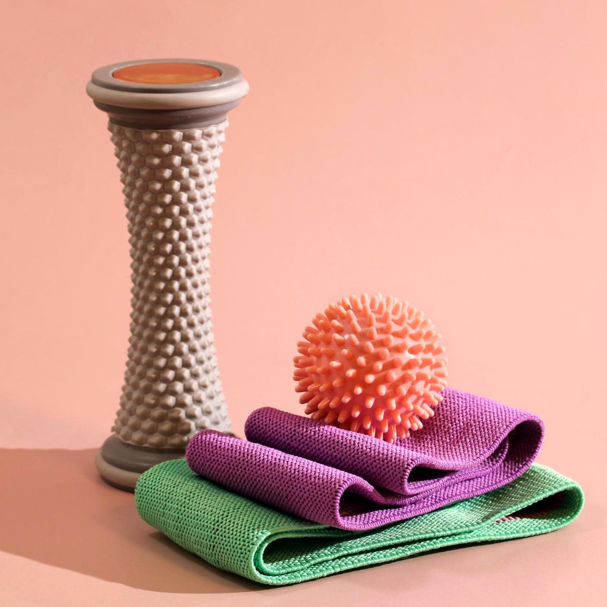 foam roller massage ball and resistance bands for muscle recovery on peach background